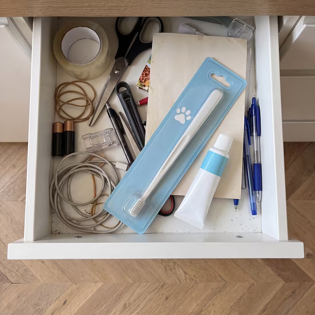 An unopened dog toothbrush and toothpaste in a kitchen junk drawer